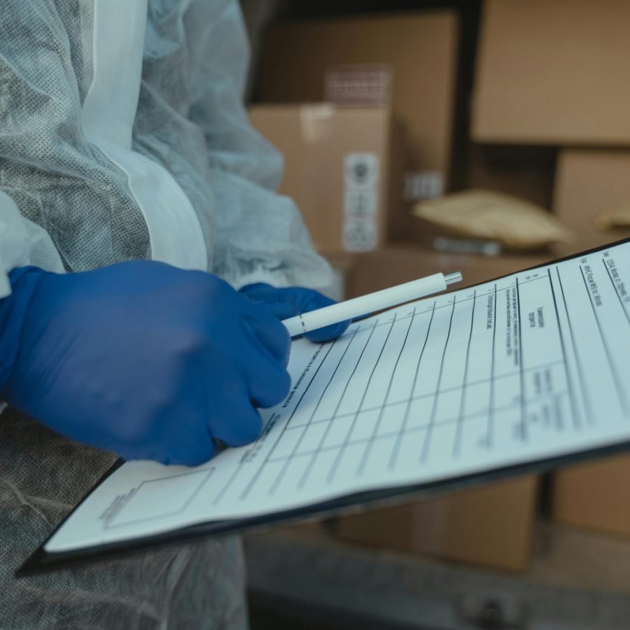 A courier wearing protective equipment writes on a clipboard among packages.